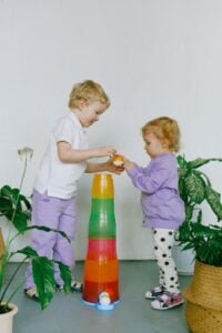 Two children playing with a tall red, green, and yellow toy